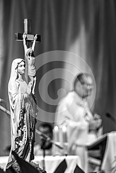 Statue of Virgin Mary with rosary, Jesus on cross and priest at background