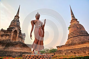 A statue of walking Buddha between Stupas in Wat Sa Si Temple at dusk in Sukhothai Historical Park