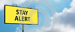 Stay Alert yellow warning sign on blue sky background. Large billboard with the message text