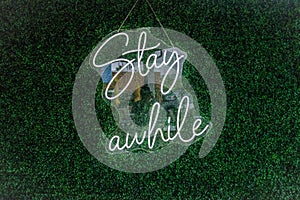 Stay Awhile Neon Sign Hanging in front of Green Background