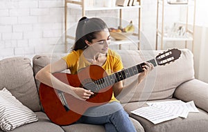 Stay home entertainment. Millennial girl learning to play acoustic guitar in apartment