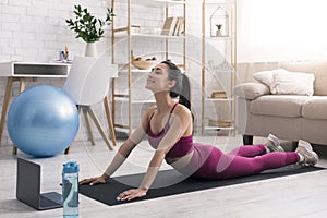 Stay at home fitness. Young girl doing back bend or snake yoga pose near laptop indoors