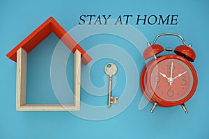Stay at home inscription on the blue background. Model of house, clock and key. Flat lay.