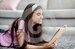 Stay home pastimes concept. Happy Indian teenage girl reading interesting book indoors