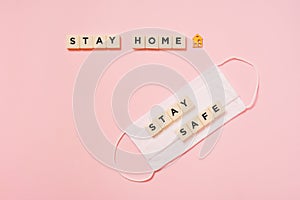 Stay home, plastic letter tiles,  with stay safe word on white fabric face mask on pink paper background