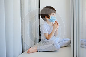 Stay at home quarantine for coronavirus pandemic prevention. Child and his teddy bear both in protective medical masks sits on