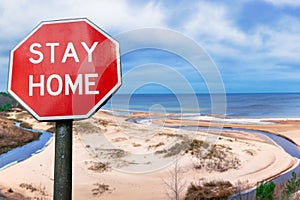 Stay home sign against view of white sand beach and sea surrounded by conifer trees forest
