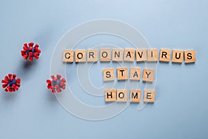 Stay home stay safe concept made up of wooden letters and models of covid-19 virus on blue background