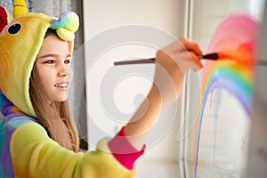 Teen girl in kigurumi draws rainbow on window home photo