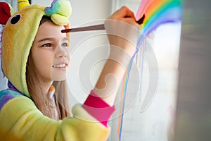 Teen in kigurumi draws rainbow on window home photo