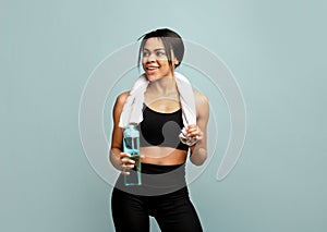 Stay hydrated. Sporty black woman in black sportswear and white towel on neck holding bottle of fresh water