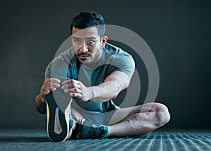 Stay limber. Full length shot of a handsome young male athlete warming up against a grey background.