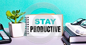 STAY PRODUCTIVE is written on a white card next to a potted flower, diaries and calculator. Organizational concept