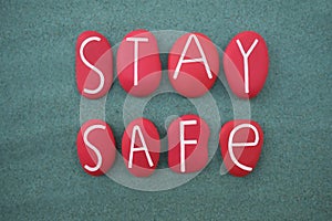 Stay Safe, creative slogan composed with red colored painted stone letters over green sand