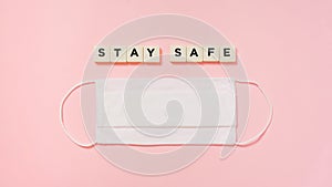 Stay safe, plastic letter tiles, and white fabric face mask on pink paper background