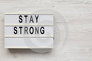 `Stay strong` on a lightbox on a white wooden surface, top view. Flat lay, overhead, from above. Copy space