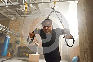 Stay strong in your life. Athletic young man doing fitness TRX training exercises at industrial gym. Push-up, group