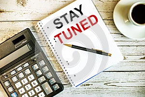 STAY TUNED written on white paper near coffee and calculator on a light wooden table. Business concept