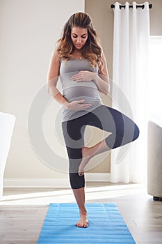 Staying active right down to her due date. a pregnant young woman practicing the tree pose during a yoga routine at home