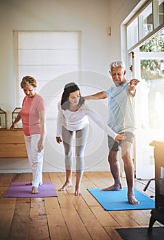 Staying balanced in their elder years. a teacher helping a senior man during a yoga class.