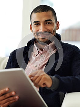Staying connected has never been easier. Portrait of a smiling young man working at home on a digital tablet.
