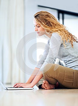 Staying connected with the ones she loves. A cute young blonde sitting on the floor and browsing her laptop.