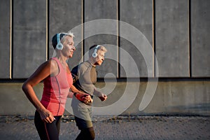 Staying fit. Happy and sporty middle-aged couple in headphones running together through the city street in the morning