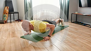 Staying fit. Mature man fitness instructor in sportswear doing push ups on yoga mat at home, exercising during self