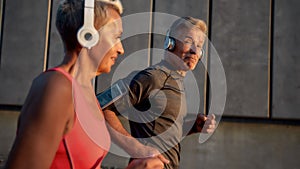 Staying fit together. Happy and healthy middle-aged couple in headphones running through the city street in the morning