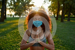 Staying healthy during coronavirus outbreak. Young mixed race woman wearing protective face mask meditating and