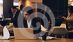 Staying late with the rest of her team. Shot of a young businesswoman going through paperwork while working on a laptop