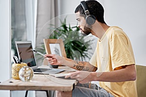 Staying in place, keeping up the business pace. a young man using a laptop and headphones while working from home.