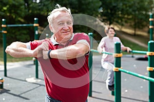 Staying after retirement. Happy joyful mature retired sportsman wearing sportswear doing side stretching exercises with