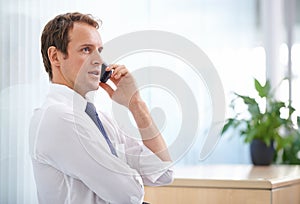 Staying in touch. a handsome businessman talking on the phone in the office.