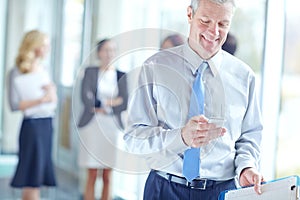 Staying in touch. A handsome mature businessman using his mobile while standing in the office.