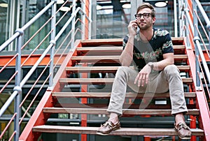 Staying in touch with his clients. Shot of a handsome young man using his mobile phone while sitting on the steps of an