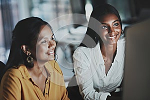 Staying up as a dedicated duo. two young businesswomen working together on a computer in an office at night.