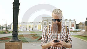 Steadicam shot of Bearded tourist man with backpack walking street and using smartphone for view map outdoors