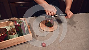 Steadicam shot: housewife closing lids on the jars with canned cherry tomatoes, with a seamer or special seaming key