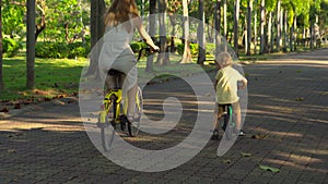 Steadycam shot of a young woman and her little son riding a bicycle and runbike in a tropical park