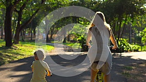 Steadycam shot of a young woman and her little son riding a bicycle and runbike in a tropical park