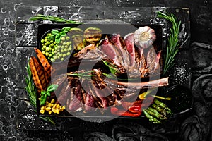 Steak on the bone. Two juicy baked veal steaks with vegetables and spices. On a black background. Top view. Free copy space