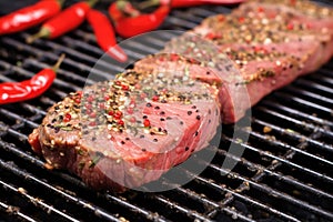 steak on grill grates with peppercorns scattered around