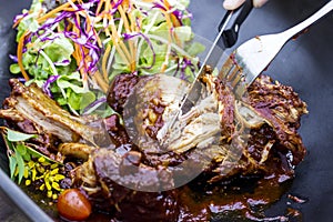 Steak knife and fork slicing grilled rib eye beef steak in black bowl