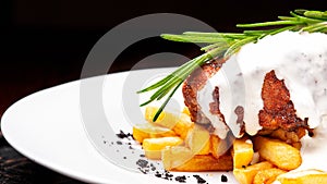 Steak medallion with French fries on a white plate. Steak is poured with white sauce
