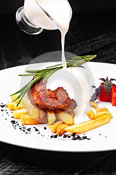 Steak medallion with French fries on a white plate. Steak is poured with white sauce