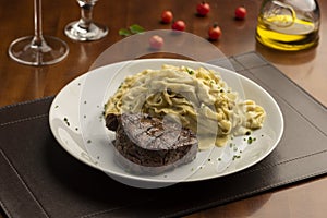 Steak with pasta tagliatelle fetuccini on plate with blurred background with tomatoes olive oil