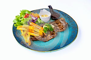 Steak pork chop topped with black pepper sauce and sausage with french fries and vegetable salad on dish with white background.
