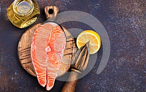 Steak of raw salmon with lemon and olive oil on a dark background Top view