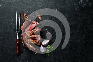 Steak Ribeye grill on fork on black stone background. Top view.